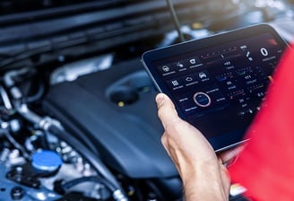 man holding a tablet analyzing a car's engine.