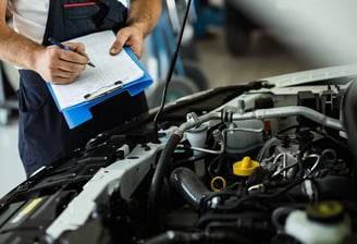 man with blue clipboard evaluating a car's engine.