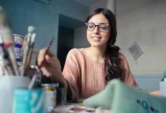 a woman in glasses and a pink sweater is sitting at a desk