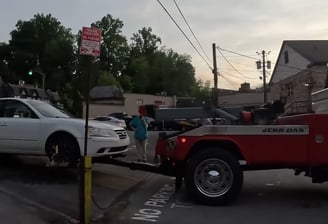 Red to truck hooking a white automobile, readying it to be towed from a parking lot.
