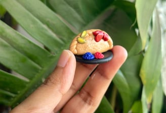 Clay gujiya-shaped fridge magnet held against a green leaf backdrop