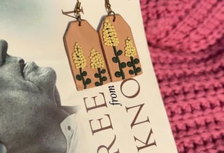 a pair of handmade yellow flower earrings displayed on a white book with pink cloth backdrop