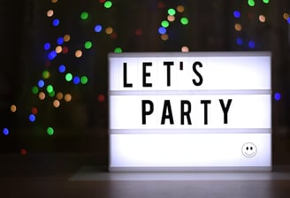 A lit sign in a darkened room that reads "Let's Party"