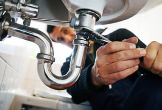 man turning a pipe under a sink with a special tool