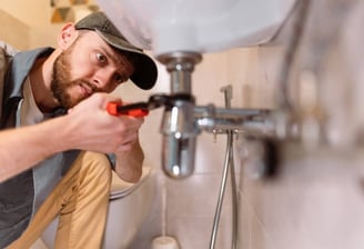 plumber focusing very hard while he is turning a pipe under a sinkj