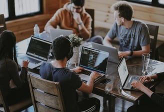 a group of people sitting around a table with laptops