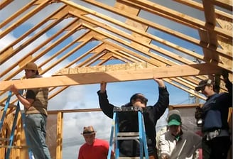 two women and a man framing the trusses of a house construction