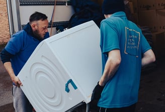a man in a blue shirt is moving a refrigerator