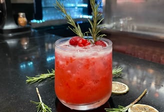 a cocktail with a sprig of rosemary on the side of a bar