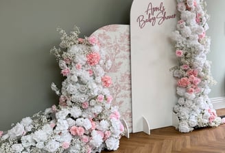 a large pink and white baby shower arch backdrop decorated with flowers
