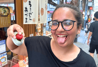 Trisha, a girl making a silly face with her tongue out and holding a Strawberry Mochi