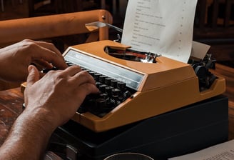 a man typing on a typewriter with a glass of wine