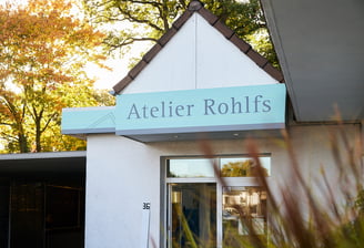 EIne außenaufnahme von einem Gebäude mit Bäumen im Hintergrund auf einem Schild steht Atelier Rohlfs