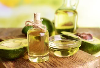 A glass bottle with a cork and twine, filled with a light golden liquid, avocado oil.