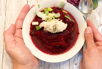 Beet soup in a while bowl with hands holding it
