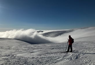 picture of one person viewing snowy fell landscape wiht clouds in valley and clear sky