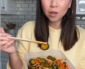 a woman holding a container with vegetables and chopsticks