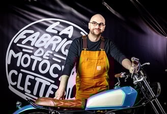 Homme barbu à lunettes en salopette jaune posant avec sa moto