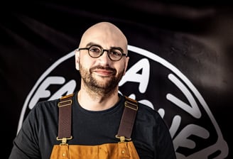 Homme avec une barbe et des lunettes posant devant une banderolle noire