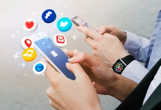 الصورة تظهر يدين تحملان هاتفاً ذكياً، ويرتدي الشخص ساعة أبل الذكية. تتطاير من الهاتف أيقونات مواقع التواصل الاجتماعي المختلفة