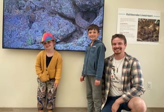 Project Rattlecam Team member, Owen, and 2 kids in front of RattleCam Zoo display