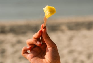 paplūdimio fone ant šakutės pasmeigtas pjaustyto ananaso gabaliukas