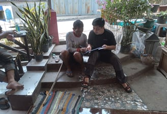 "Peneliti dan warga komunitas lokal berdiskusi bersama di ruang terbuka, merekam pengetahuan budaya 