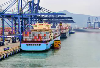 Container ship docking at sea port with cargo cranes and containers in background.