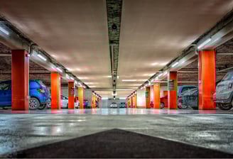 Underground parking lot with orange columns and smart lighting under surveillance system.