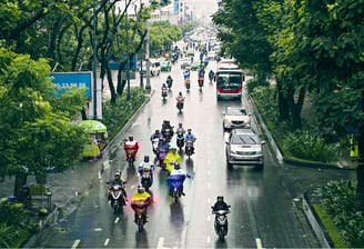 Urban road with motorbikes and cars in rainy conditions managed by smart traffic control systems.