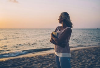 Mujer joven en la playa, abrazando un libro