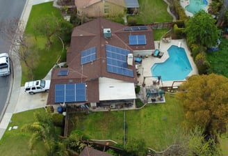 Aerial view of a house with solar panels on the roof and a pool in the backyard, showcasing a modern