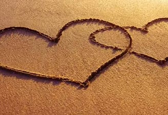 two hearts in the sand with a heart shaped drawing on the sand