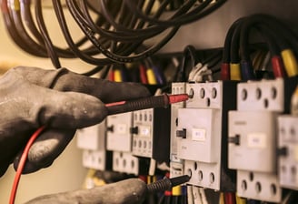 a person holding a wire and wires in front of a wall mounted electrical equipment