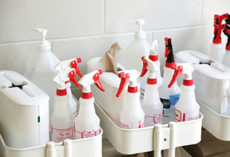 Estante de baño con varios pulverizadores y botellas de limpieza de color blanco y etiquetas rojas