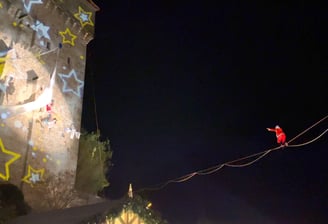 Le pere Noel marche en equilibre sur un fil en direction de mere noel suspendue a un tissu