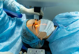 Paciente em sala cirúrgica realizando procedimento oftalmológico a laser com uso de touca e máscara
