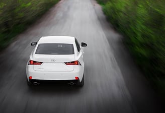 a white car driving down a road with trees in the background