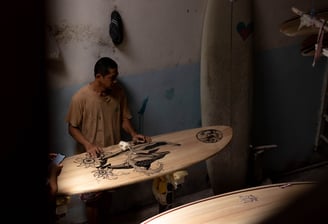 Craftsman shaping a handmade balsa surfboard with intricate artwork