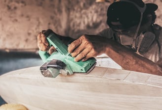 Craftsman shaping a handmade balsa surfboard with an electric planer