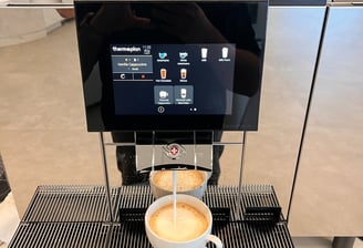 Thermoplan Black&White 4c espresso machine preparing a cappuccino with a touchscreen interface.