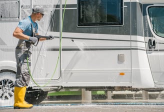 A man in yellow boots is pressure washing an RV