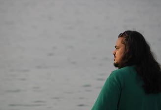 ध्यानपूर्ण मुद्रा में समुद्र की ओर देखते हुए एक व्यक्ति – आत्म-चिंतन और शांति की झलक