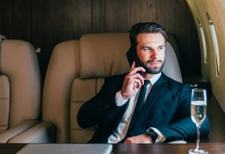 Homem sentado na poltrona do avião na classe executiva ao telefone e degustando um champagne