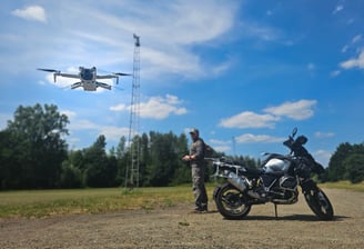 Drone stijgt op voor inspectievlucht terwijl piloot toezicht houdt, naast adventuremotor op open terrein