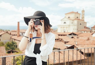  "A traveling woman wearing a stylish hat holding a camera, ready to capture travel moments. 