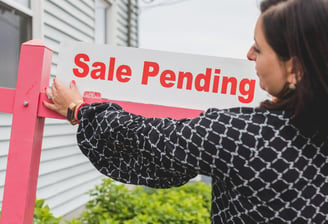 "A real estate agent placing a 'Sale Pending' sign in front of a home, symbolizing a successful sale