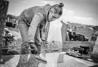Personne nettoyant une pierre tombale avec une raclette dans un cimetière