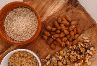 A wooden cutting board topped with a variety of raw nuts used in traditional Panjeeri preparation.