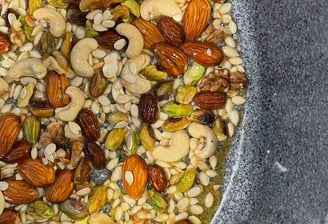A pan of assorted nuts frying in desi ghee, the base preparation for traditional Panjeeri